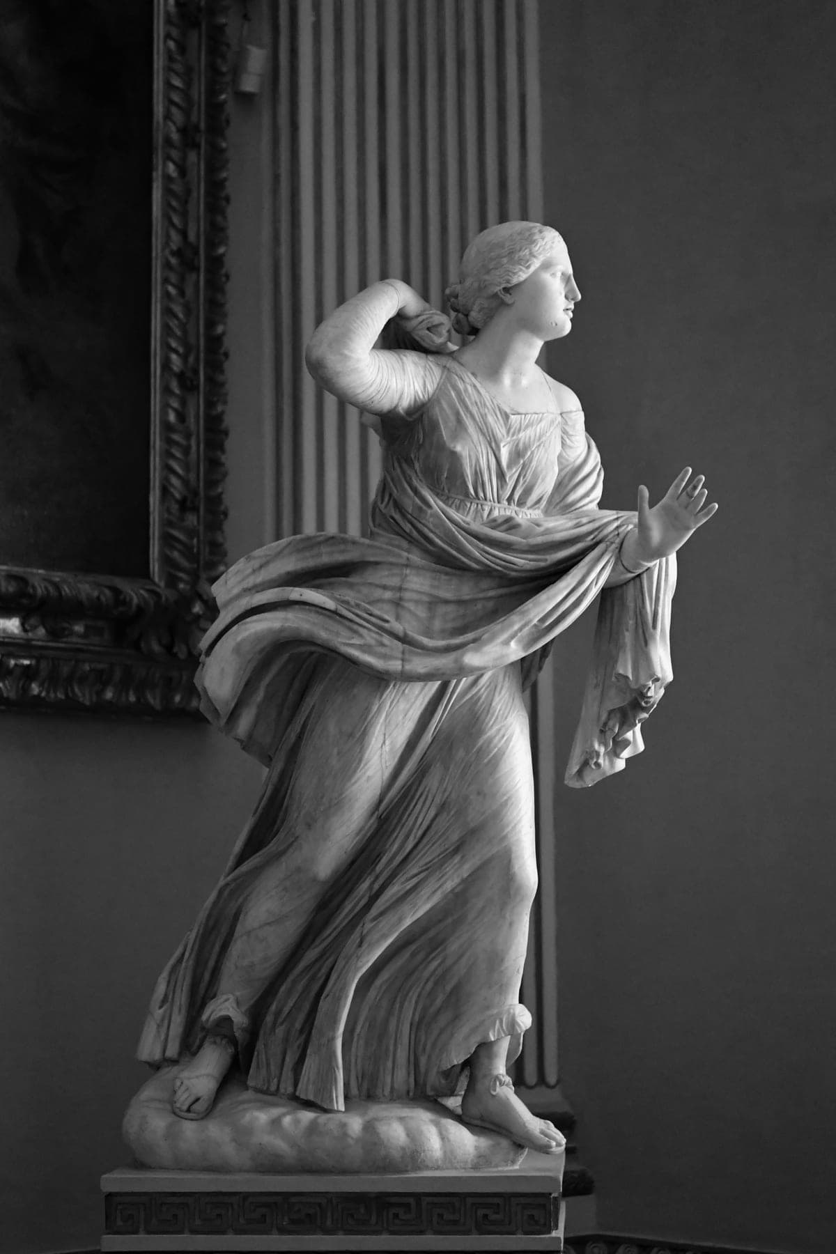 Classical marble statue of a draped female figure in motion, one hand raised — suggesting action, clarity, and purpose rather than passive beauty